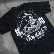 Load image into Gallery viewer, close up, angled image of the back of a black mineral wash tee shirt on a concrete background. tee has a back print in white of a skeleton opening up a coffin. below that says bayside bury me