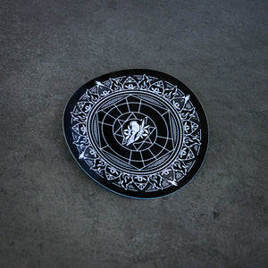image of a sticker that is a circle with a mandella and a bird design. laid flat on a concrete background.