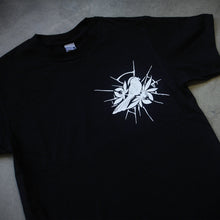 Load image into Gallery viewer, angled image of the front of a black tee shirt laid flatg on a concrete floor. tee has a small right chest print of a bird.
