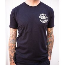 Load image into Gallery viewer, image of man from the neck down with tattoos on both arms wearing black tee shirt in front of a white background. the right breast area of the tee says 21 years of bad luck in a circle around a bird on leaves in cream print.