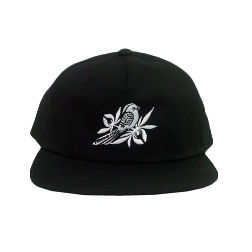 image of a black snapback on a white background. hat has white embroidery of a bird with leaves