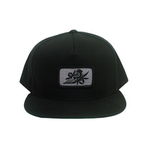Load image into Gallery viewer, image of a black snapback hat on a white background. hat has small rectangle patch sewn on the front center. patch is grey with a black bird