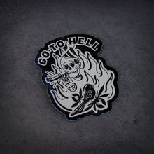 Load image into Gallery viewer, image of a sticker that says go to hell and has a skeleton smoking a joint and the bird on it. laid flat on a concrete floor