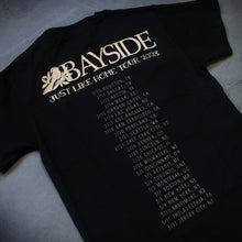 Load image into Gallery viewer, image of the back of a black tee shirt laid flat on a concrete floor. tee has the dates and locations of their 2023 tour