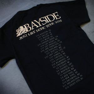 image of the back of a black tee shirt laid flat on a concrete floor. tee has the dates and locations of their 2023 tour