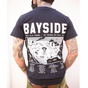 image of a man with white background from the next down with tattoos on his neck and both arms that are in his pockets. facing away showing the back of a black t shirt with a full back print in white. the top of the t shirt says bayside at the top, 21 U S tour, 21 years of bad luck with a map of the USA and tour dates on the bottom