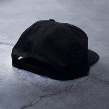 Load image into Gallery viewer, back side of a black snap back hat on a concrete background
