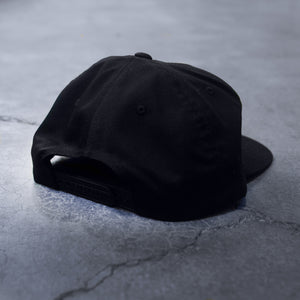 back side of a black snap back hat on a concrete background