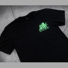 Load image into Gallery viewer, close up, angled image of the front of a black tee shirt on a concrete background. tee has a small chest print on the right in green of a bird and below the bird says bayside.