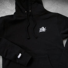 Load image into Gallery viewer, image of a black pullover hoodie laid flat on a concrete floor. small white embroidered bird on the right chest and a small sewn on patch that says bayside on the left sleeve