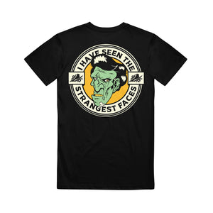 image of the back of a black tee shirt on a white background. tee  has a print of a green, zombie face. around the face says i have seen the strangest faces