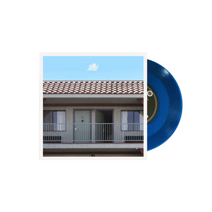 image of a blue 7 inch vinyl record coming out of the sleeve on the right side on a white background. the sleeve cover has a light blue top and an image of the outside of a motel containing a roof, two doors and a balcony.